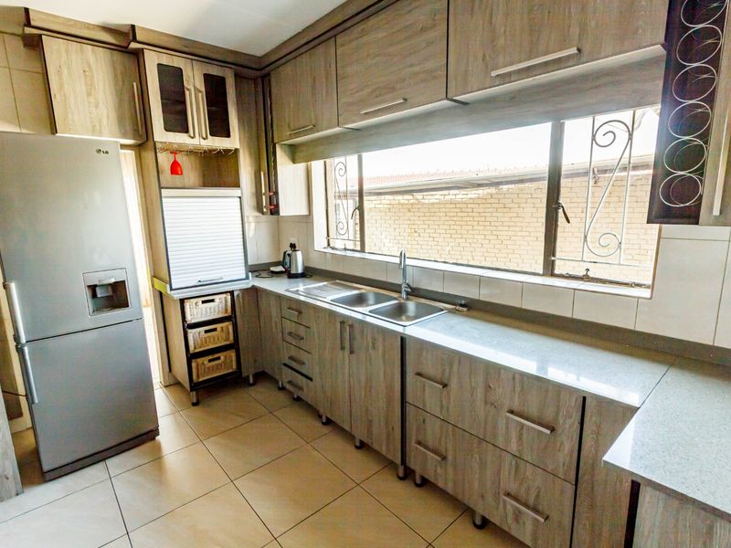 A functional kitchen featuring wood-look laminate cabinetry, stone countertops, a double basin sink, and tiled flooring with natural light from a large window.