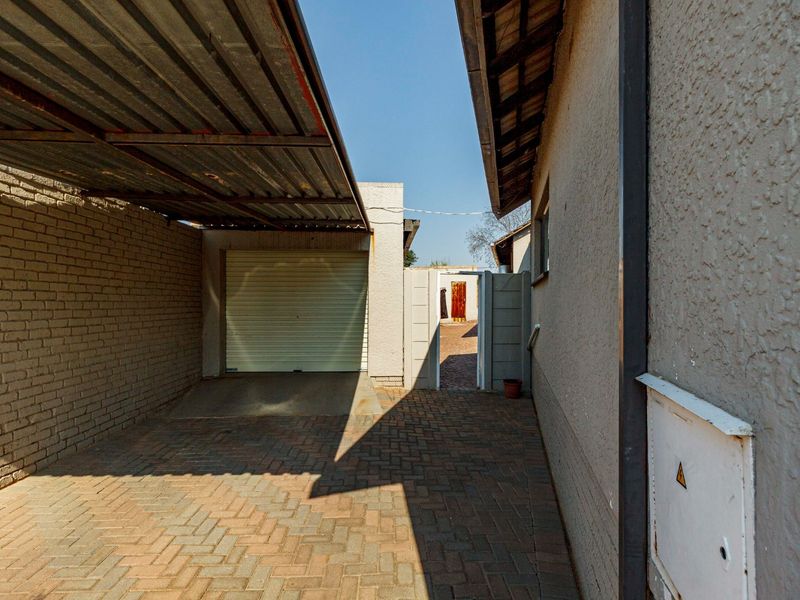 A covered carport area featuring a roller shutter garage door, paved flooring, and brick wall construction.