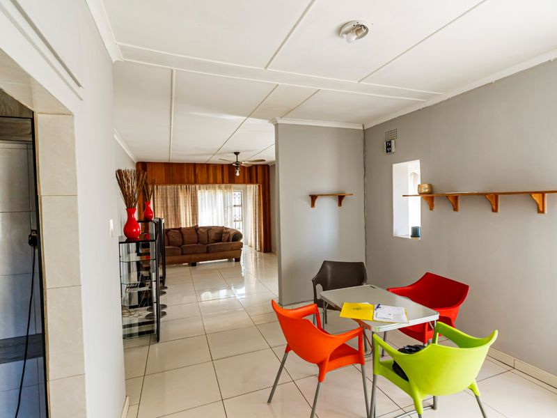 Open-plan living and dining area featuring tiled flooring, ceiling fan, and wall-mounted shelving, offering a versatile space for family living.