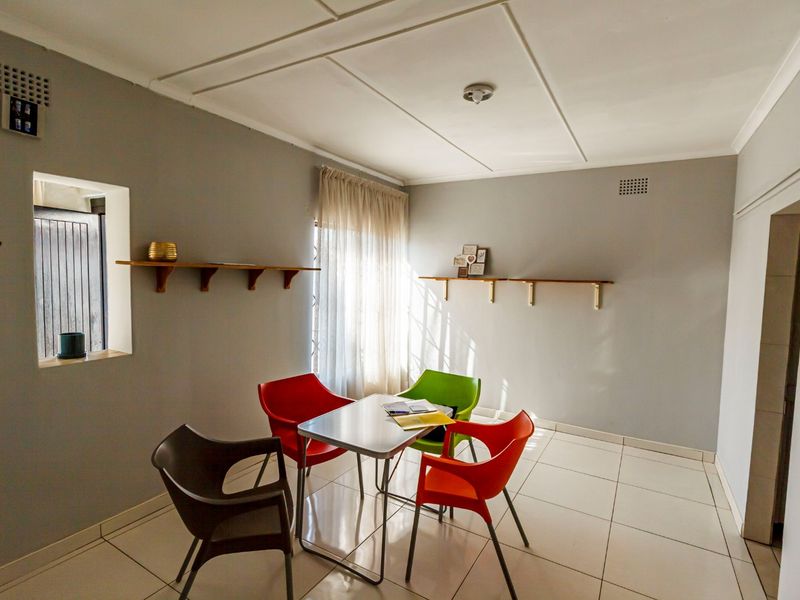 A bright dining area featuring neutral grey walls, tiled flooring, and wall-mounted shelving, offering a clean and functional space for meals.