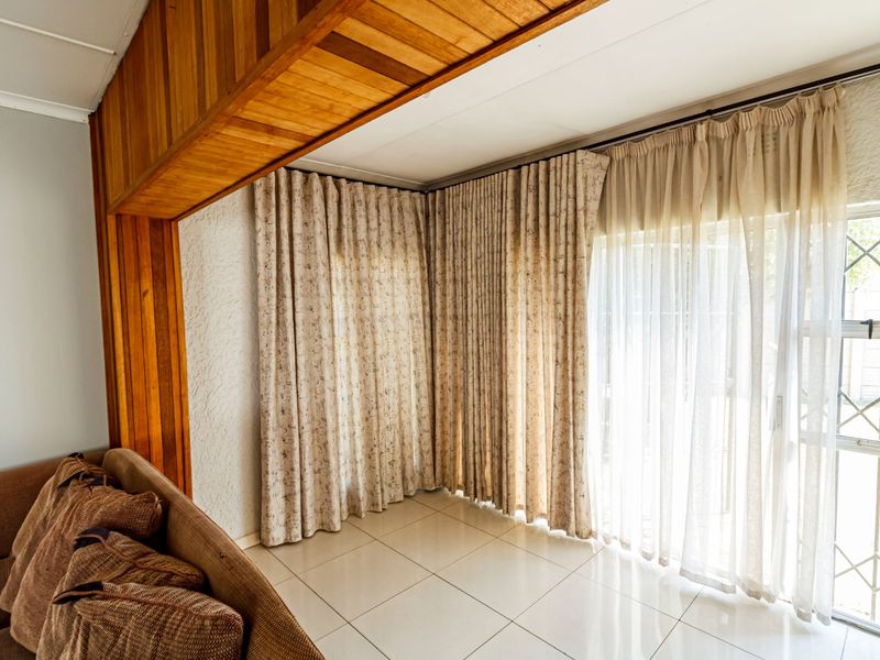 Living area featuring tiled flooring, a decorative timber ceiling beam, and large sliding glass doors with security gates leading to the exterior.