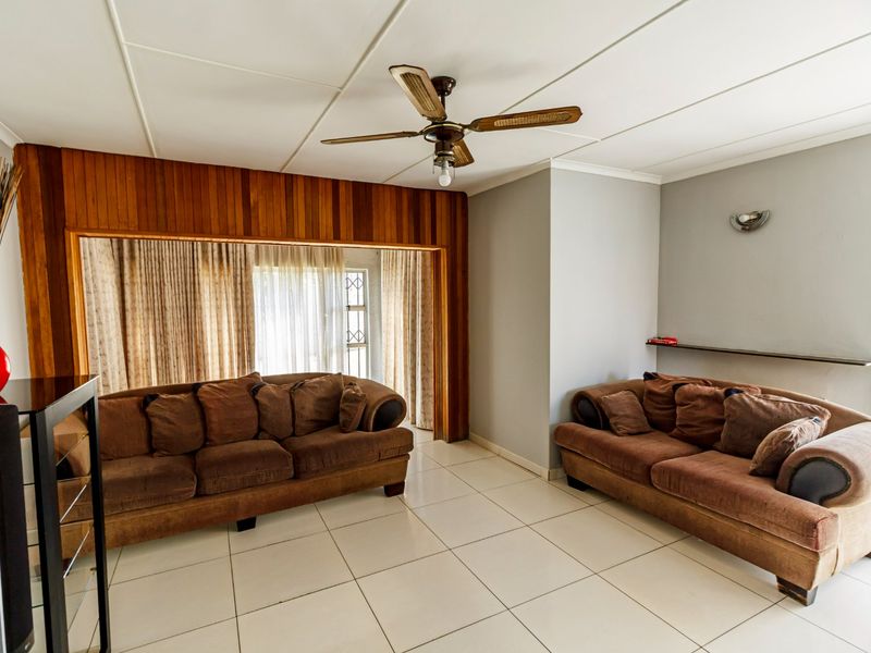 A living room featuring tiled flooring, a ceiling fan, and decorative timber wall paneling, offering a functional space with neutral wall finishes.