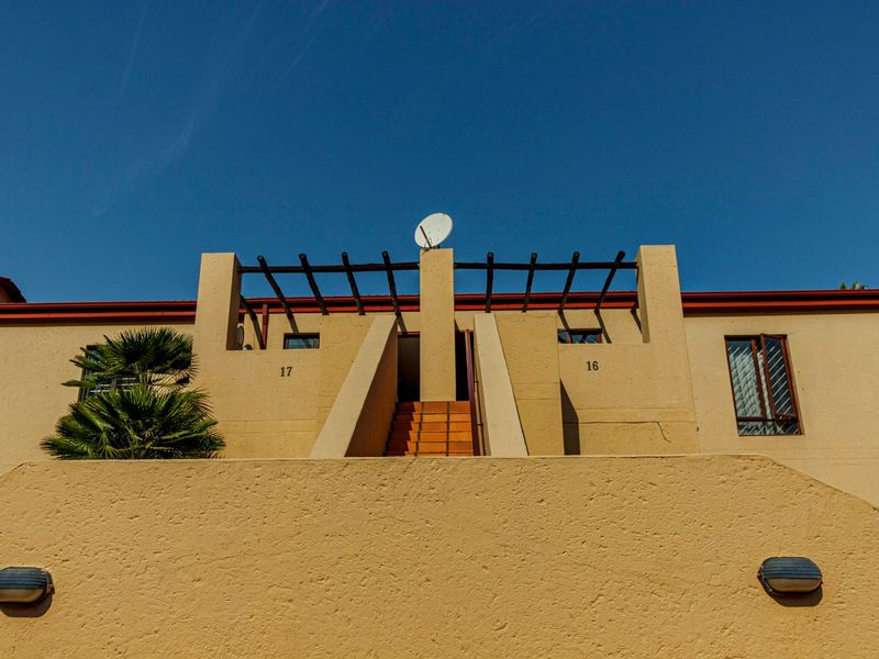 Front elevation of a townhouse complex featuring a central staircase, pergola structure, and exterior wall lighting.