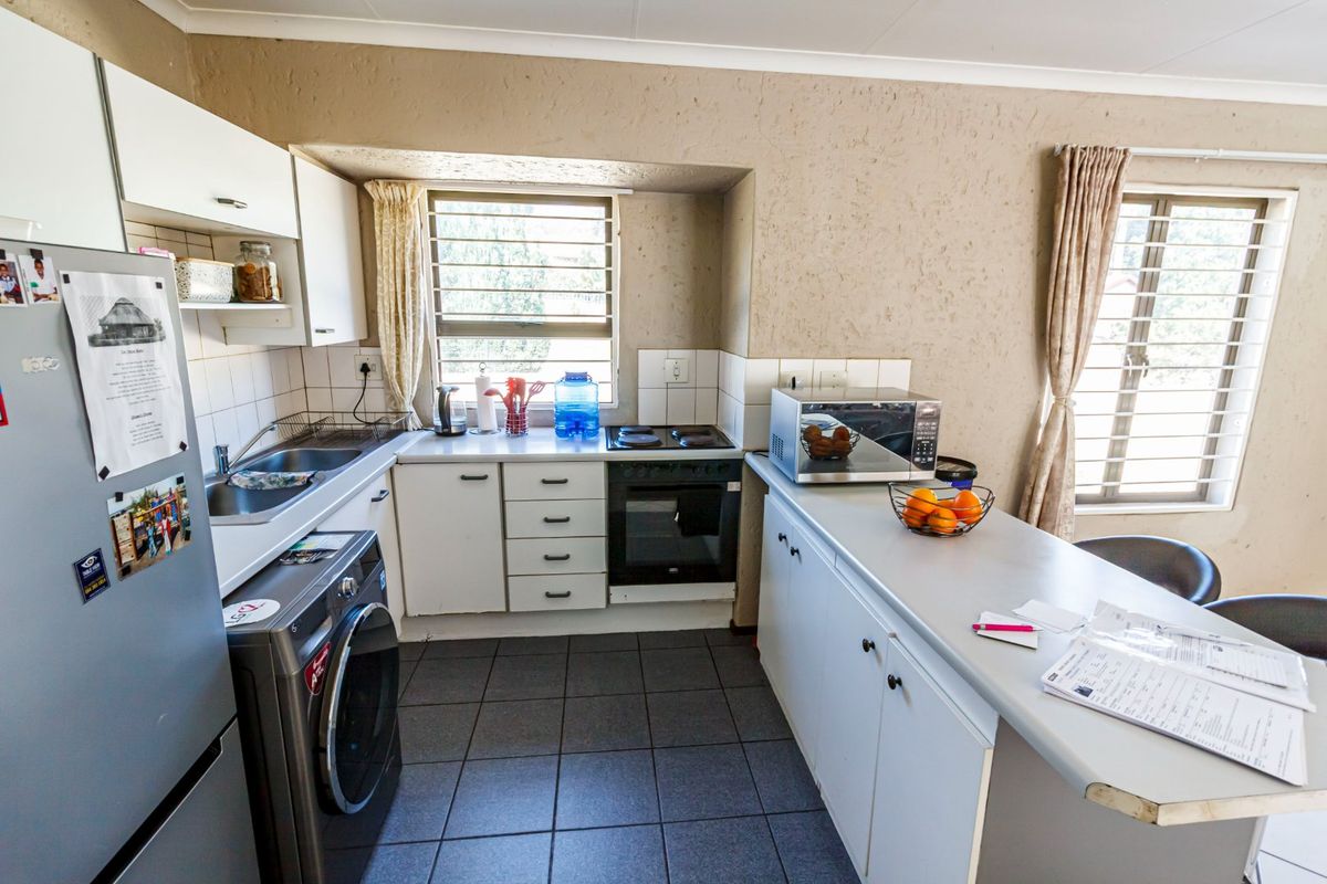 A functional kitchen featuring built-in cabinetry, tiled backsplash, electric oven and hob, and tiled flooring with security bars on the windows.