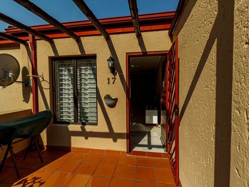 Front entrance area featuring a terracotta tiled patio, timber pergola structure, and security gate access to the townhouse interior.
