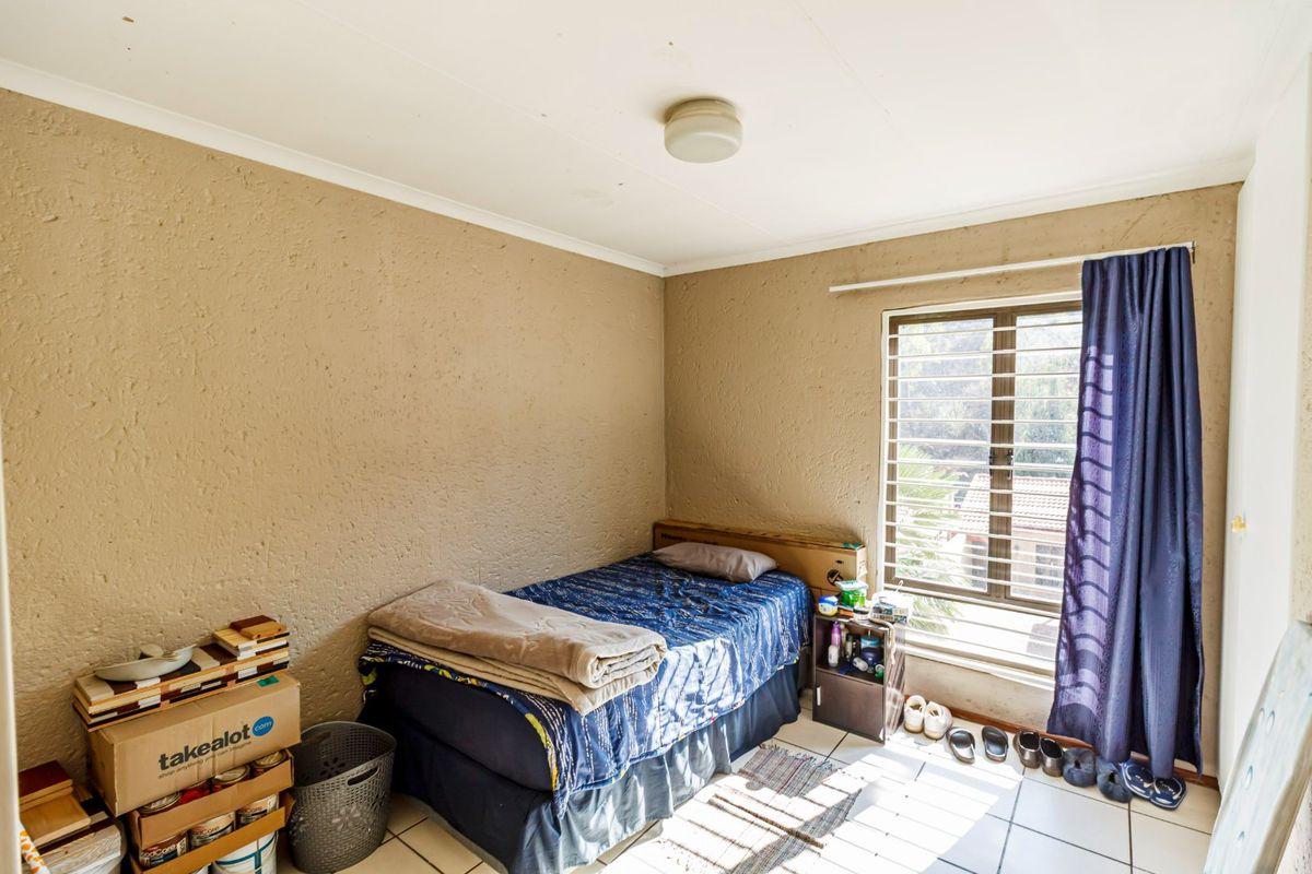 A bedroom featuring tiled flooring, textured walls, and a window fitted with security bars, offering a functional space ready for updates.