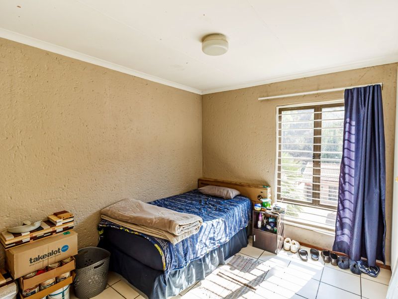 A bedroom featuring tiled flooring, textured walls, and a window fitted with security bars, offering a functional space ready for updates.