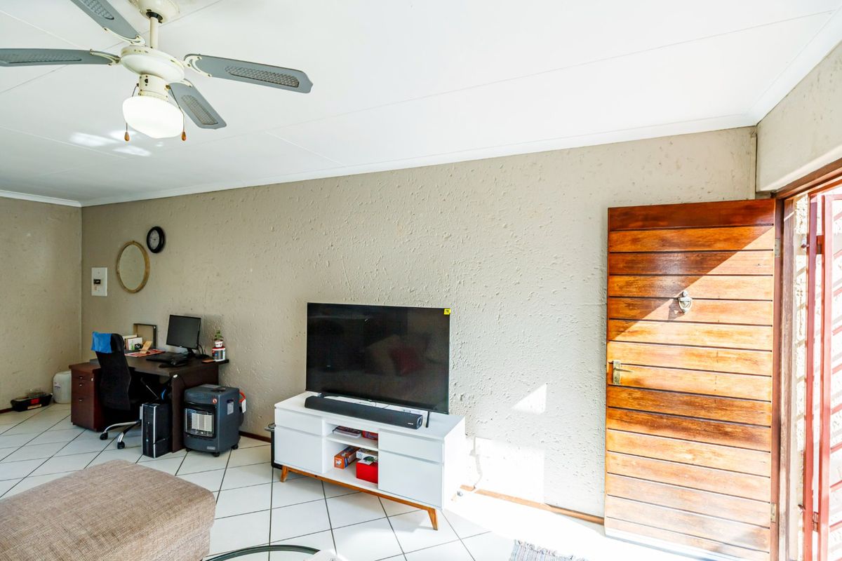 A living room area featuring tiled flooring, a ceiling fan, and a wooden door leading to the exterior.
