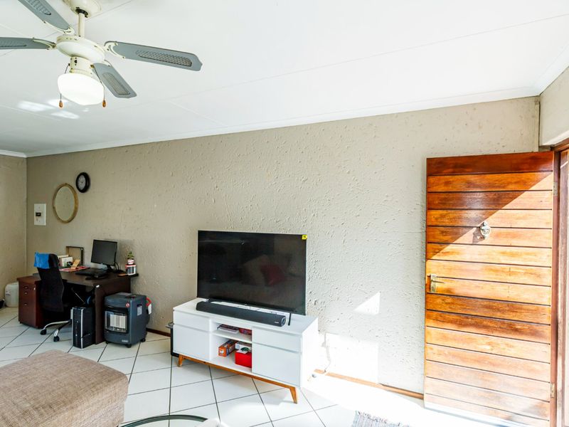 A living room area featuring tiled flooring, a ceiling fan, and a wooden door leading to the exterior.