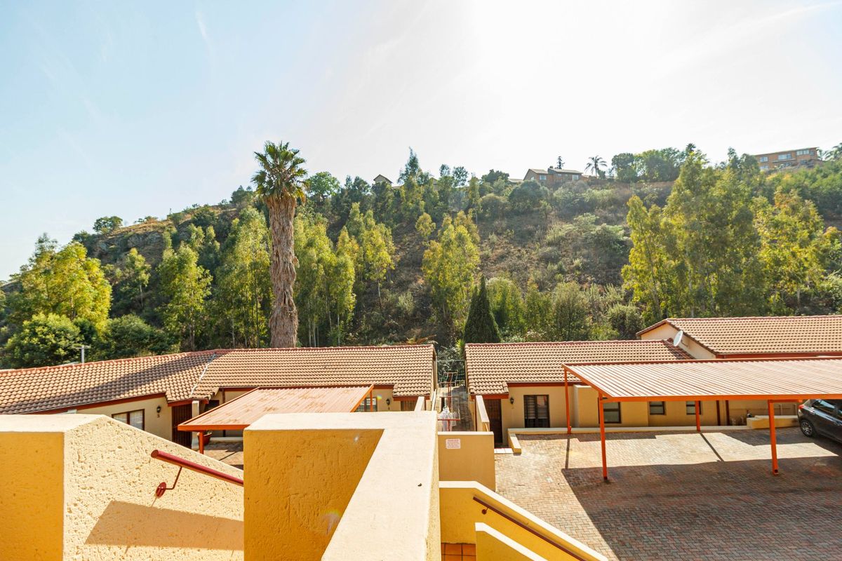 Elevated view of the townhouse complex exterior, featuring tiled roofs, paved parking areas, and covered carports set against a hillside backdrop.