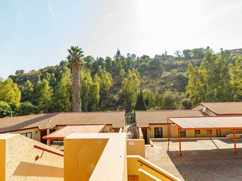 Elevated view of the townhouse complex exterior, featuring tiled roofs, paved parking areas, and covered carports set against a hillside backdrop.