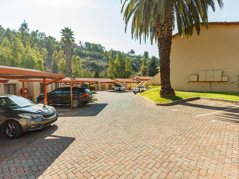 Exterior view of the townhouse complex featuring a paved driveway, covered carport parking, and established garden landscaping.