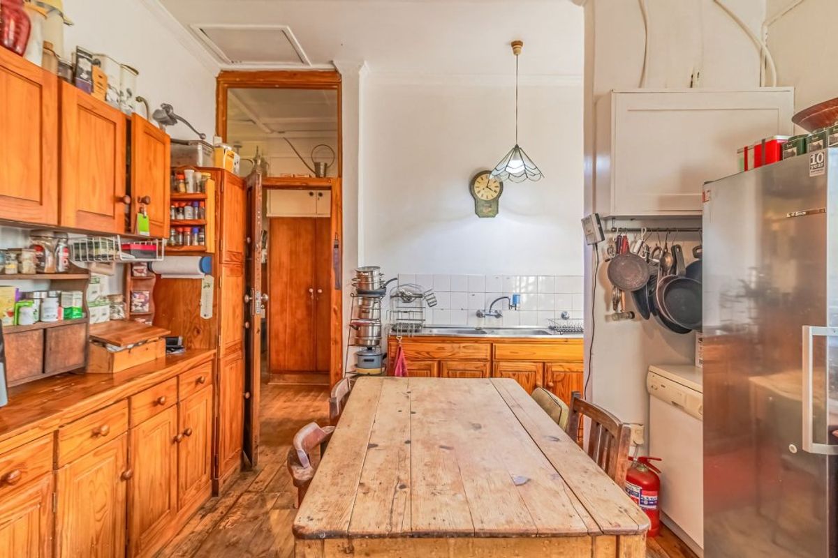 A dated kitchen featuring timber cabinetry, a double bowl sink, tiled splashback, and original timber flooring, offering significant potential for a modern renovation.