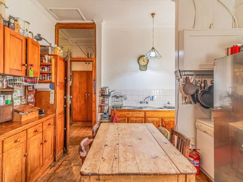 A dated kitchen featuring timber cabinetry, a double bowl sink, tiled splashback, and original timber flooring, offering significant potential for a modern renovation.