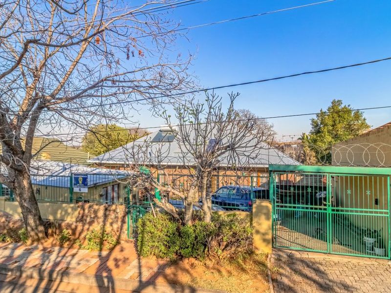 Front exterior view of the property featuring a paved driveway, secure metal gate with razor wire, and a corrugated metal roof with solar geyser.
