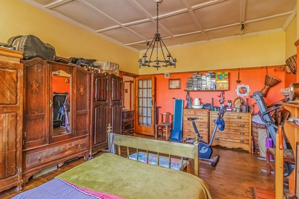 Spacious bedroom featuring original hardwood flooring, a coffered ceiling, and a classic wrought iron chandelier, offering a traditional aesthetic with potential for modernization.