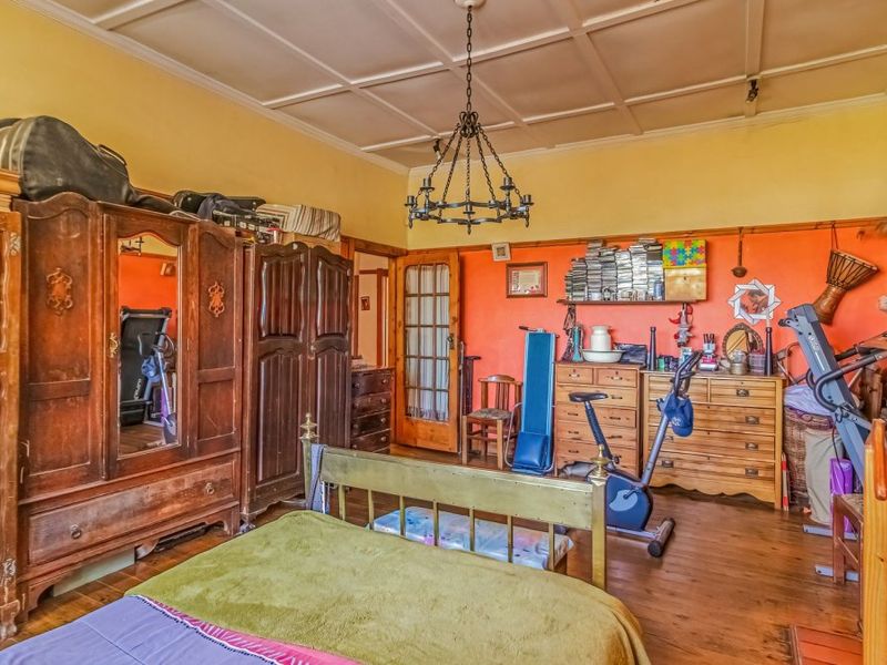 Spacious bedroom featuring original hardwood flooring, a coffered ceiling, and a classic wrought iron chandelier, offering a traditional aesthetic with potential for modernization.