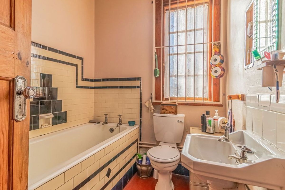A compact, dated bathroom featuring a built-in bathtub with decorative tiling, a pedestal washbasin, and a toilet, requiring cosmetic updates.