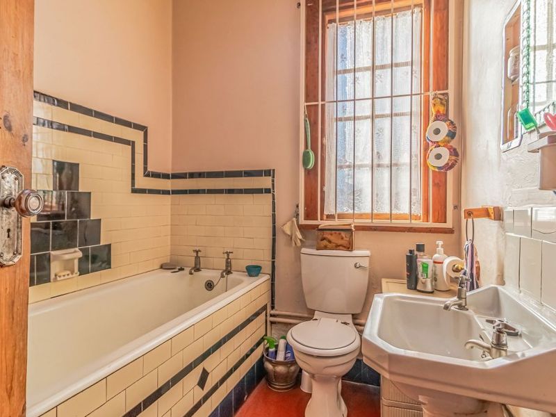 A compact, dated bathroom featuring a built-in bathtub with decorative tiling, a pedestal washbasin, and a toilet, requiring cosmetic updates.