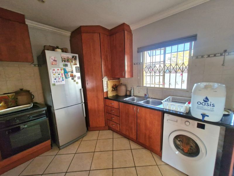 A functional kitchen featuring wooden cabinetry, tiled flooring, a double basin sink, and built-in cooking appliances with security bars on the window.