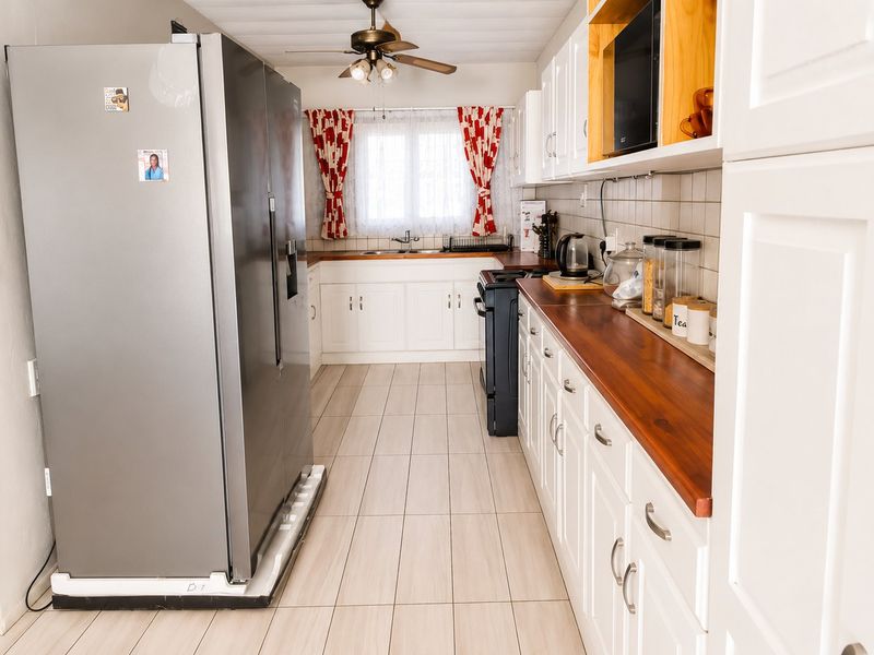 A functional kitchen featuring white cabinetry, warm wooden countertops, tiled flooring, and a double sink, offering a classic and practical layout.