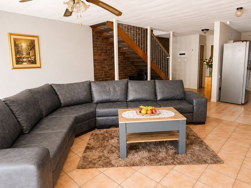 Open-plan living area featuring tiled floors, an exposed brick staircase, and a connected kitchen space with neutral cabinetry.