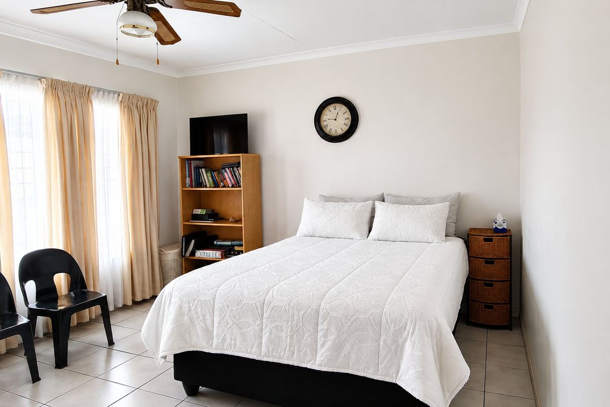 A functional bedroom featuring tiled flooring, a ceiling fan, and large windows with curtain tracks, providing a neutral base for personalization.