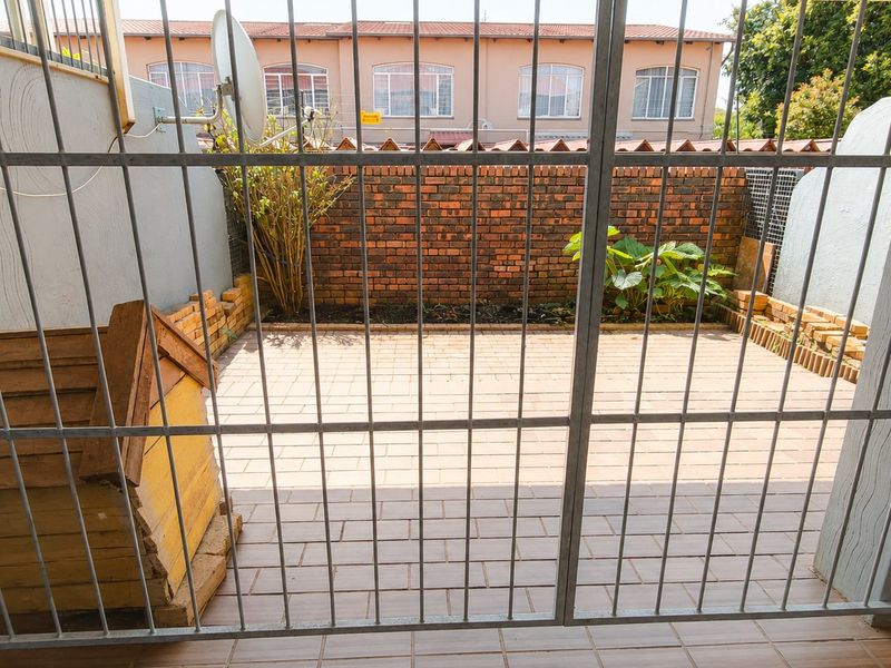 A private, paved rear courtyard enclosed by a brick boundary wall and secured with a metal gate.