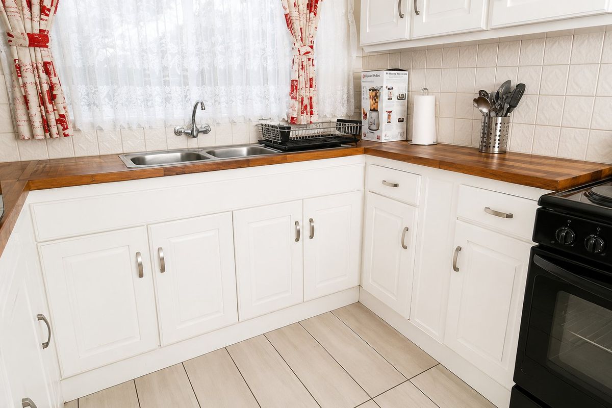 A functional kitchen featuring white cabinetry, wooden countertops, a double bowl sink, and a tiled backsplash with a freestanding electric stove.