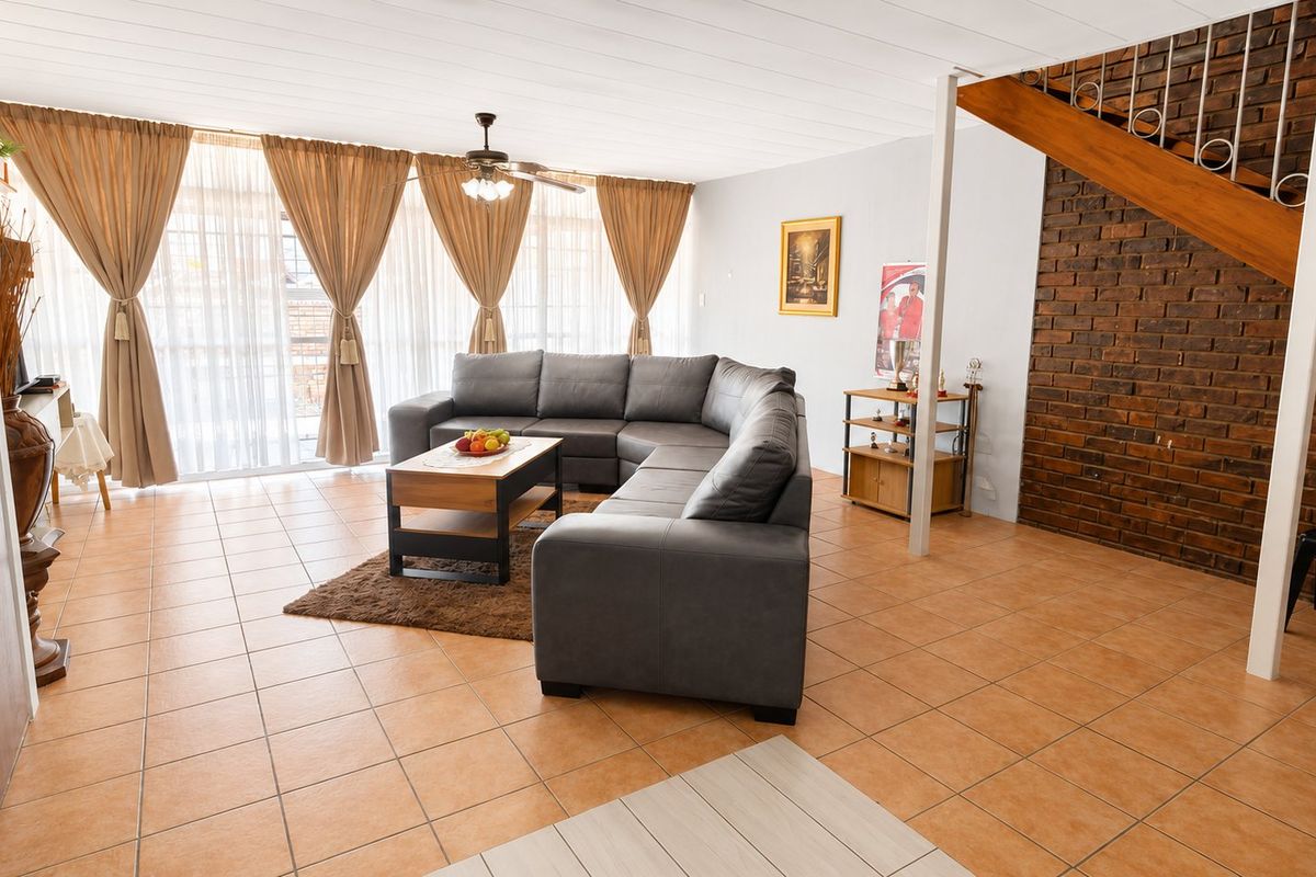Spacious living room featuring tiled flooring, an exposed brick feature wall, and a timber staircase, with large sliding doors providing ample natural light.