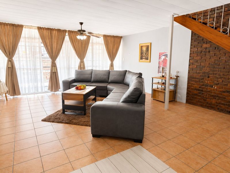 Spacious living room featuring tiled flooring, an exposed brick feature wall, and a timber staircase, with large sliding doors providing ample natural light.