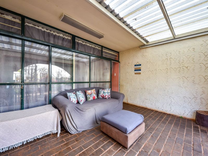 Covered patio area featuring brick flooring, a corrugated roof, and a large glass-enclosed wall, offering a versatile outdoor living space.