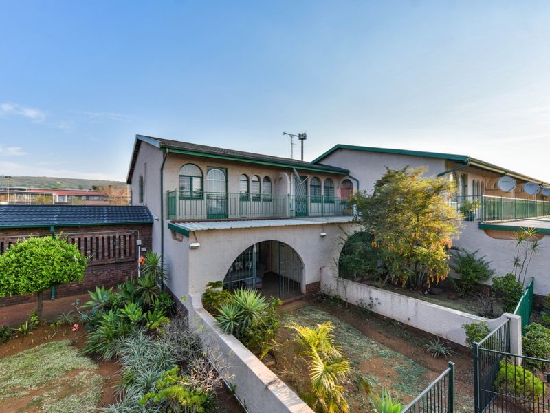 Rear view of a townhouse featuring an arched ground-floor patio, an upper-level balcony with metal railings, and a private garden area.