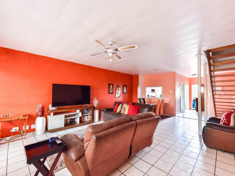Open plan living area featuring tiled flooring, a ceiling fan, and an exposed brick staircase leading to the upper level.