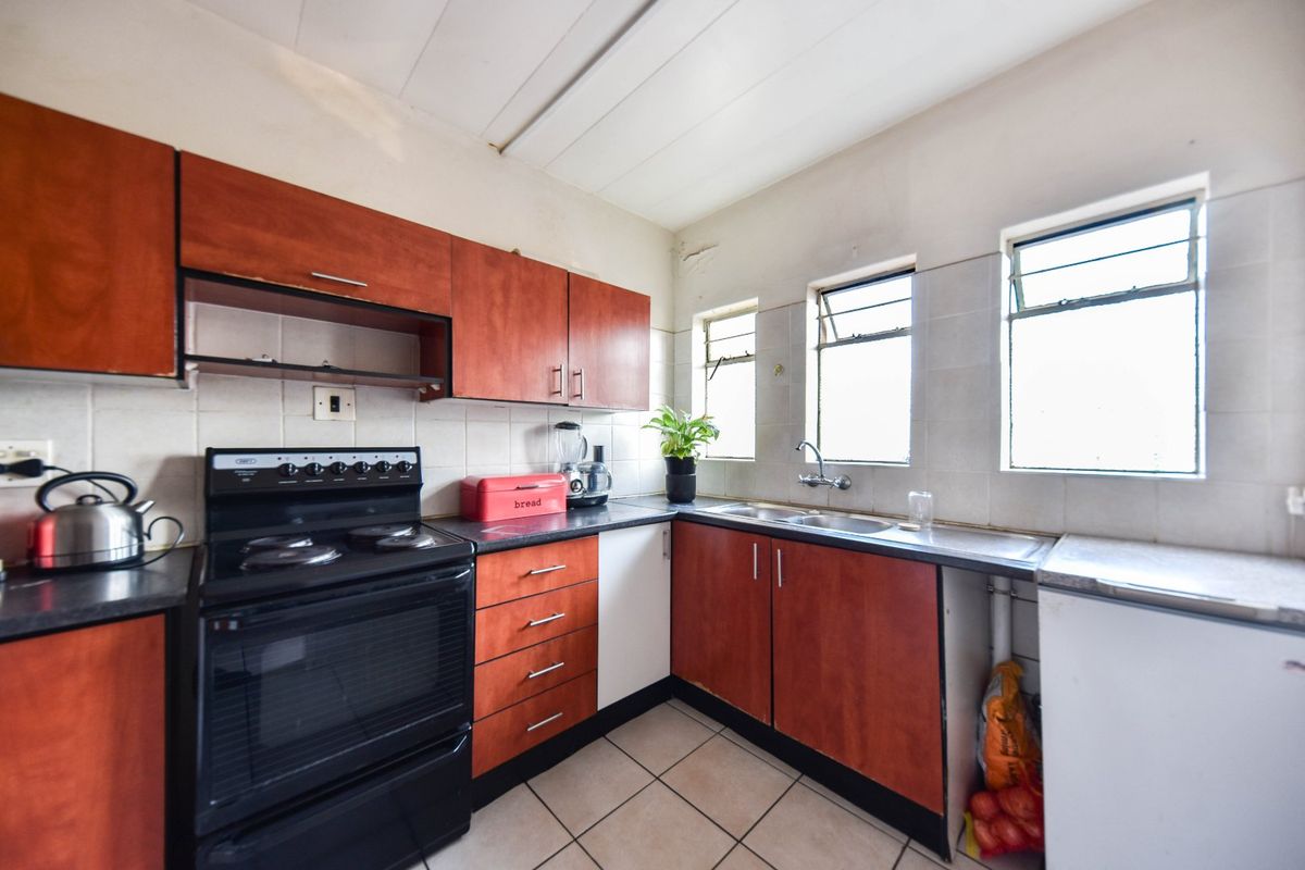 A dated kitchen featuring wood-look cabinetry, tiled backsplash, and ceramic flooring, offering a functional layout with potential for modern renovation.
