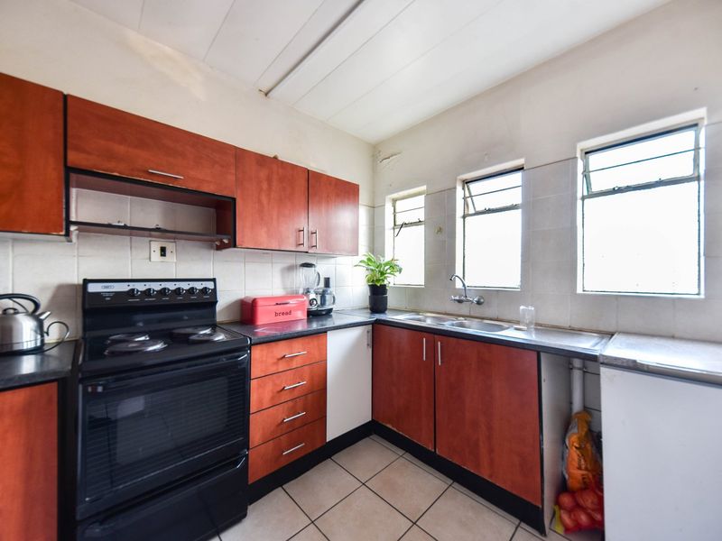A dated kitchen featuring wood-look cabinetry, tiled backsplash, and ceramic flooring, offering a functional layout with potential for modern renovation.