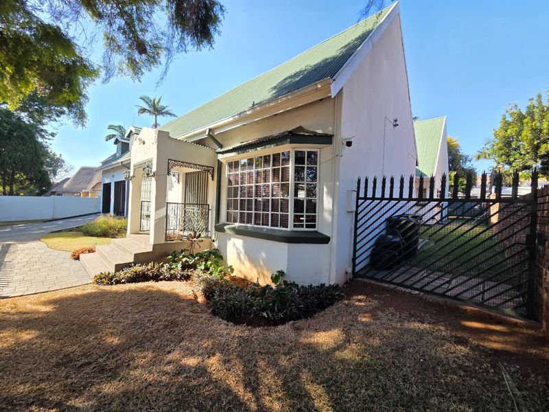 Front view of a charming house featuring a pitched roof, bay window, paved driveway, and secure gated entrance with established garden landscaping.