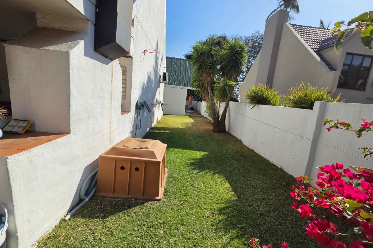 A side garden area featuring a lawn, boundary wall, and a built-in braai structure attached to the main house exterior.