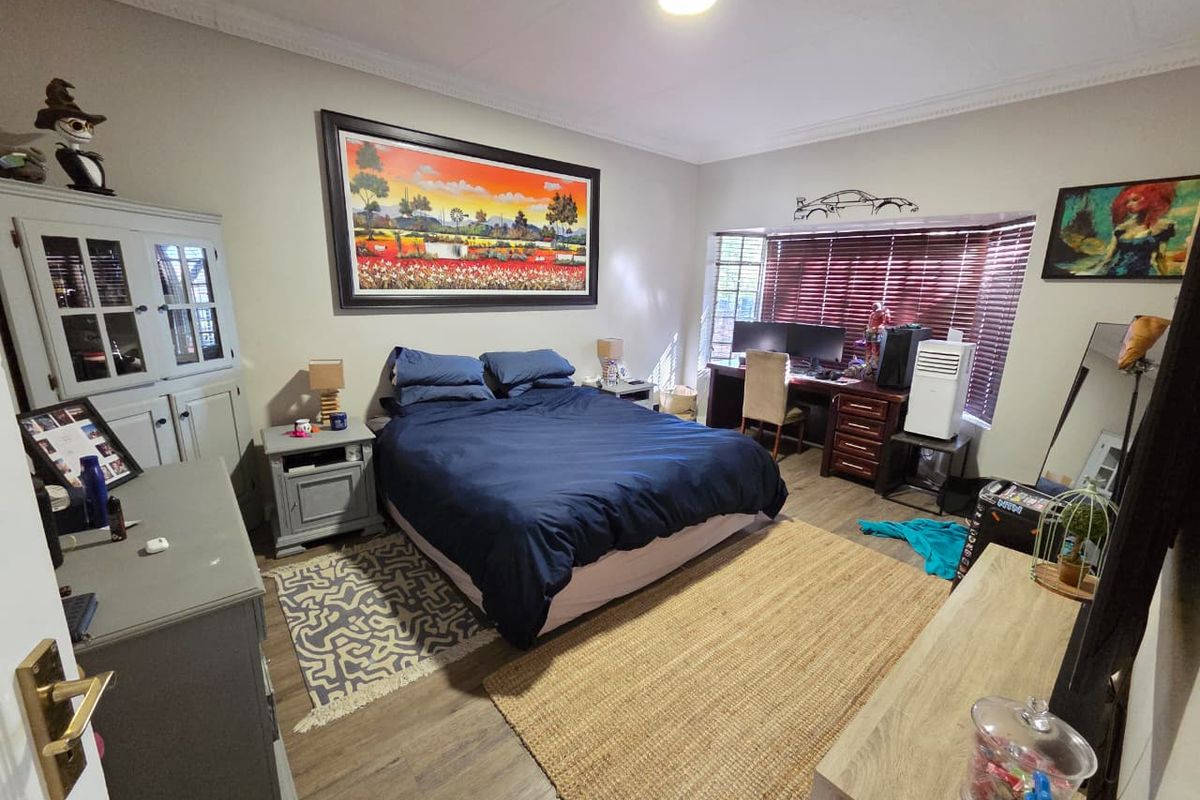 A spacious bedroom featuring laminate flooring, a large bay window with blinds, and decorative ceiling cornicing.