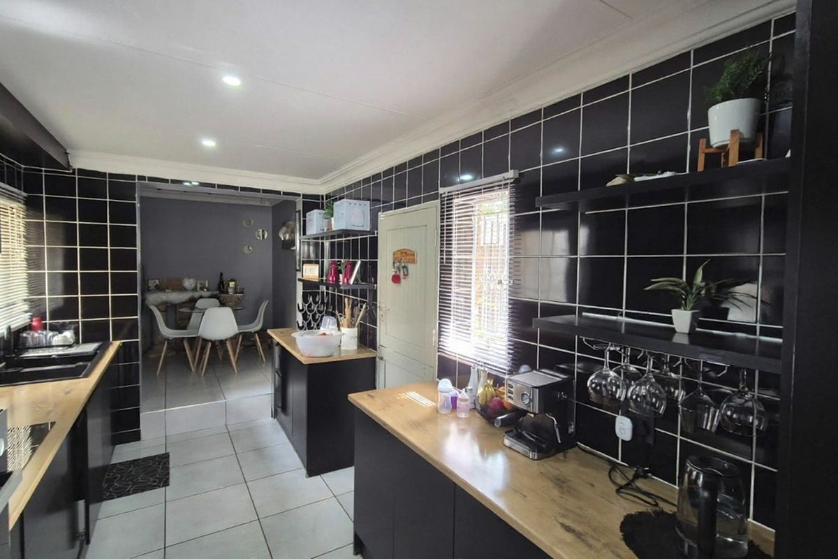 Modern kitchen featuring black tiled walls, wooden countertops, built-in appliances, and open shelving, with an adjacent dining area visible.
