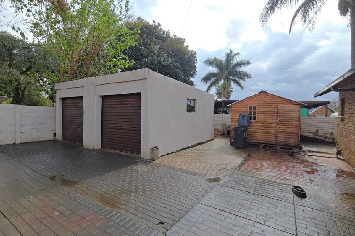 Rear exterior view featuring a double garage with roller shutter doors, paved driveway, and a detached wooden storage shed.