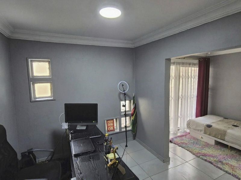 A multi-functional bedroom space featuring tiled flooring, coved ceilings, and a partitioned area with access to a patio through a security gate.