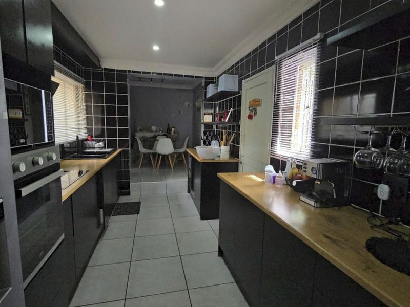 Modern kitchen featuring dark cabinetry, wooden countertops, black tiled backsplash, and built-in oven, leading into an adjacent dining area.