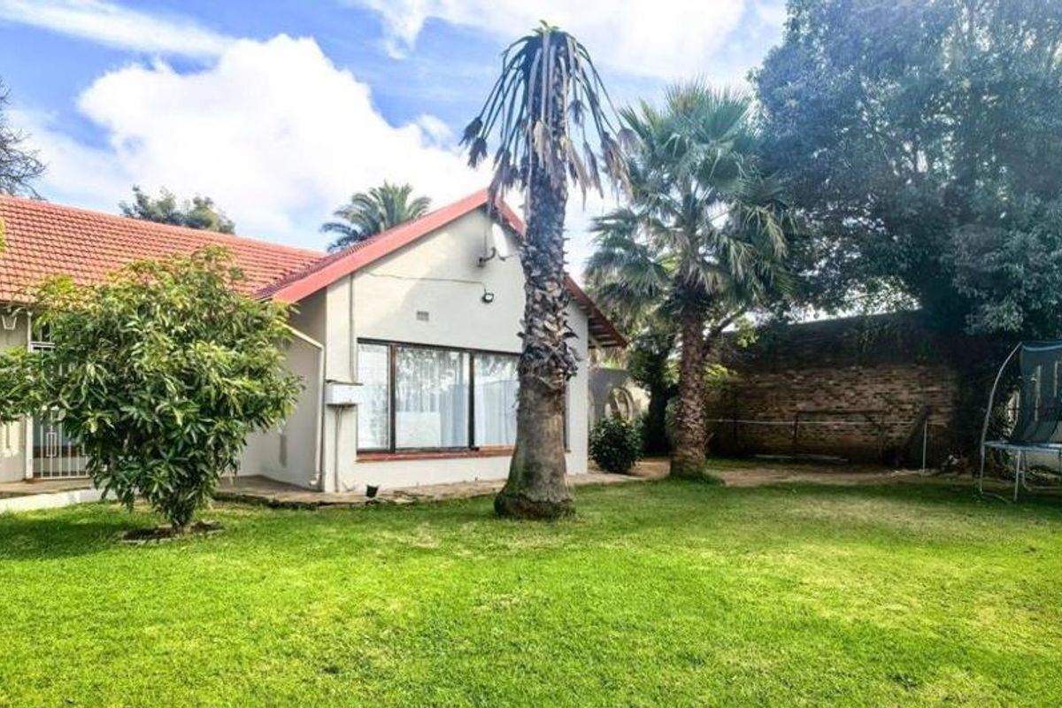 Rear view of the house featuring a spacious garden, tiled roof, and large sliding doors providing access to the outdoor area.