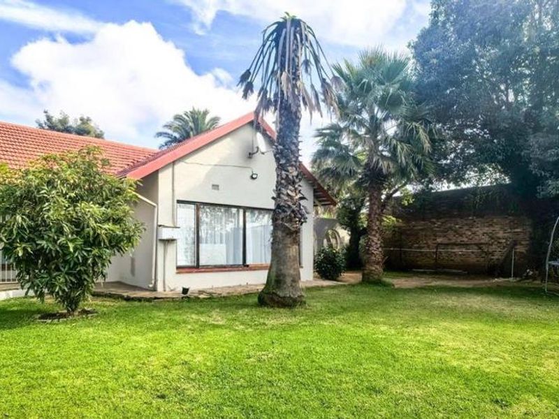 Rear view of the house featuring a spacious garden, tiled roof, and large sliding doors providing access to the outdoor area.