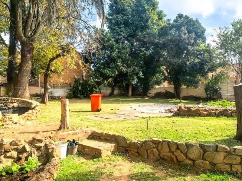 A spacious backyard featuring mature trees, stone retaining walls, and a large lawn area enclosed by a precast concrete boundary wall.