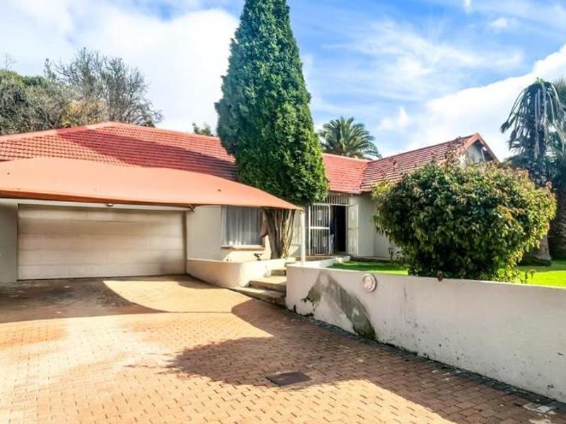 Front exterior view of the house featuring a paved driveway, shade sail, garage, and a boundary wall with established garden.