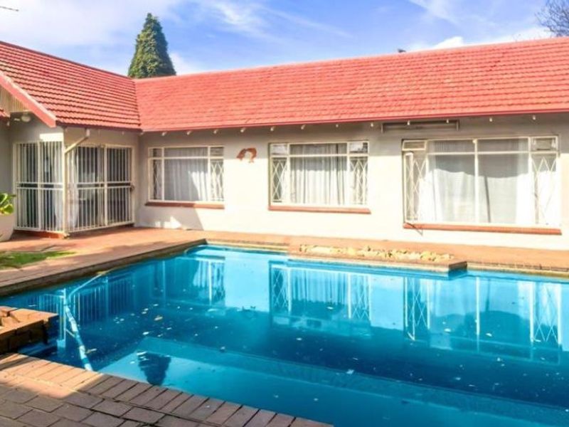 Rear exterior view of the house featuring a swimming pool, brick paved patio area, and a tiled roof structure.