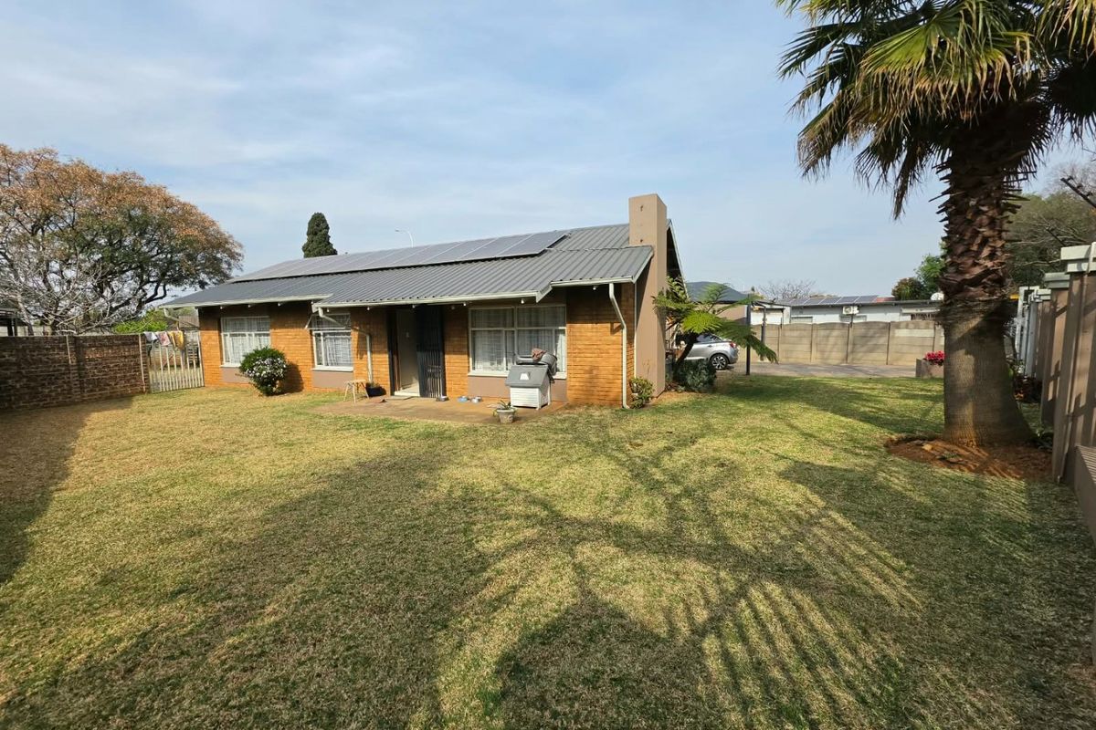 Rear view of a brick house featuring a metal roof with installed solar panels, a paved patio area, and a spacious garden.