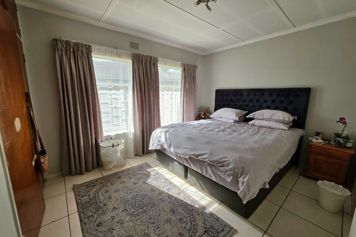 A bedroom featuring tiled flooring, neutral wall tones, and window security bars, providing a functional space with potential for cosmetic updates.